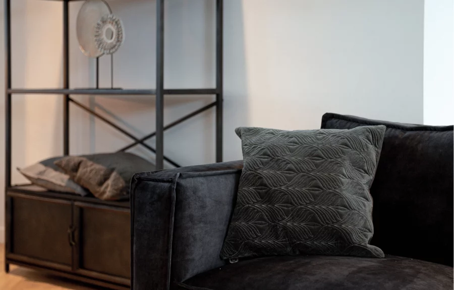 Black couch with pillow in front of open cupboard with decor