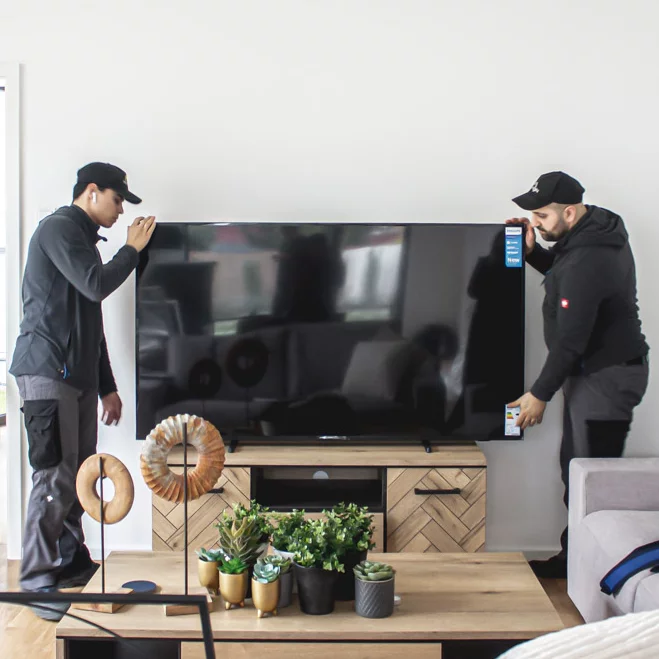 Two men carrying a flat screen TV into a living room